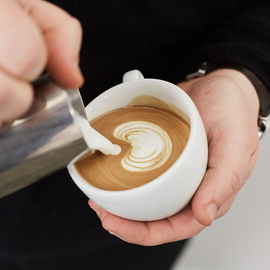 Barista vertiendo leche para crear arte en un latte.